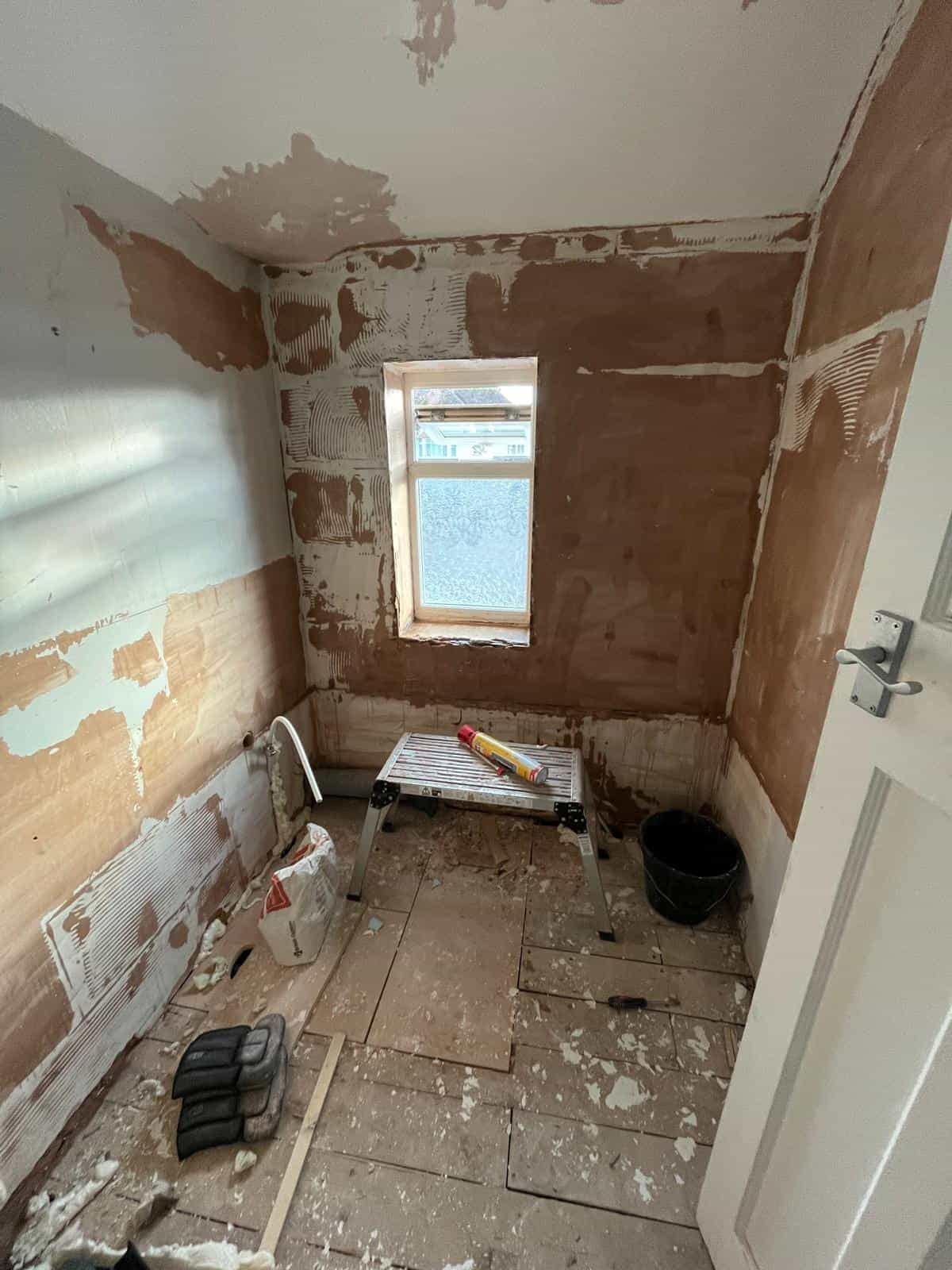 Home Small bathroom stripped back during renovation, with exposed wall surfaces, a bare floor, construction debris and a narrow window