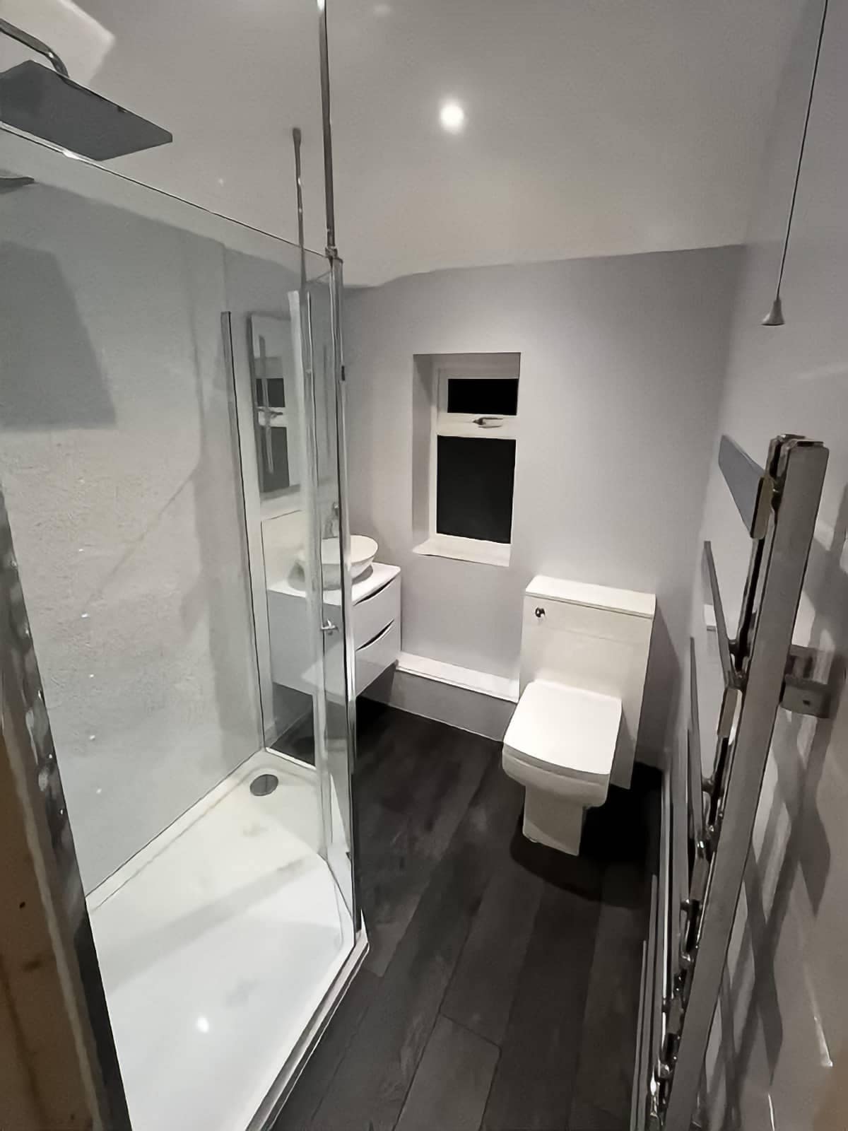 Home Completed small bathroom with shower enclosure, white vanity unit, toilet, light grey walls and dark wood-effect flooring