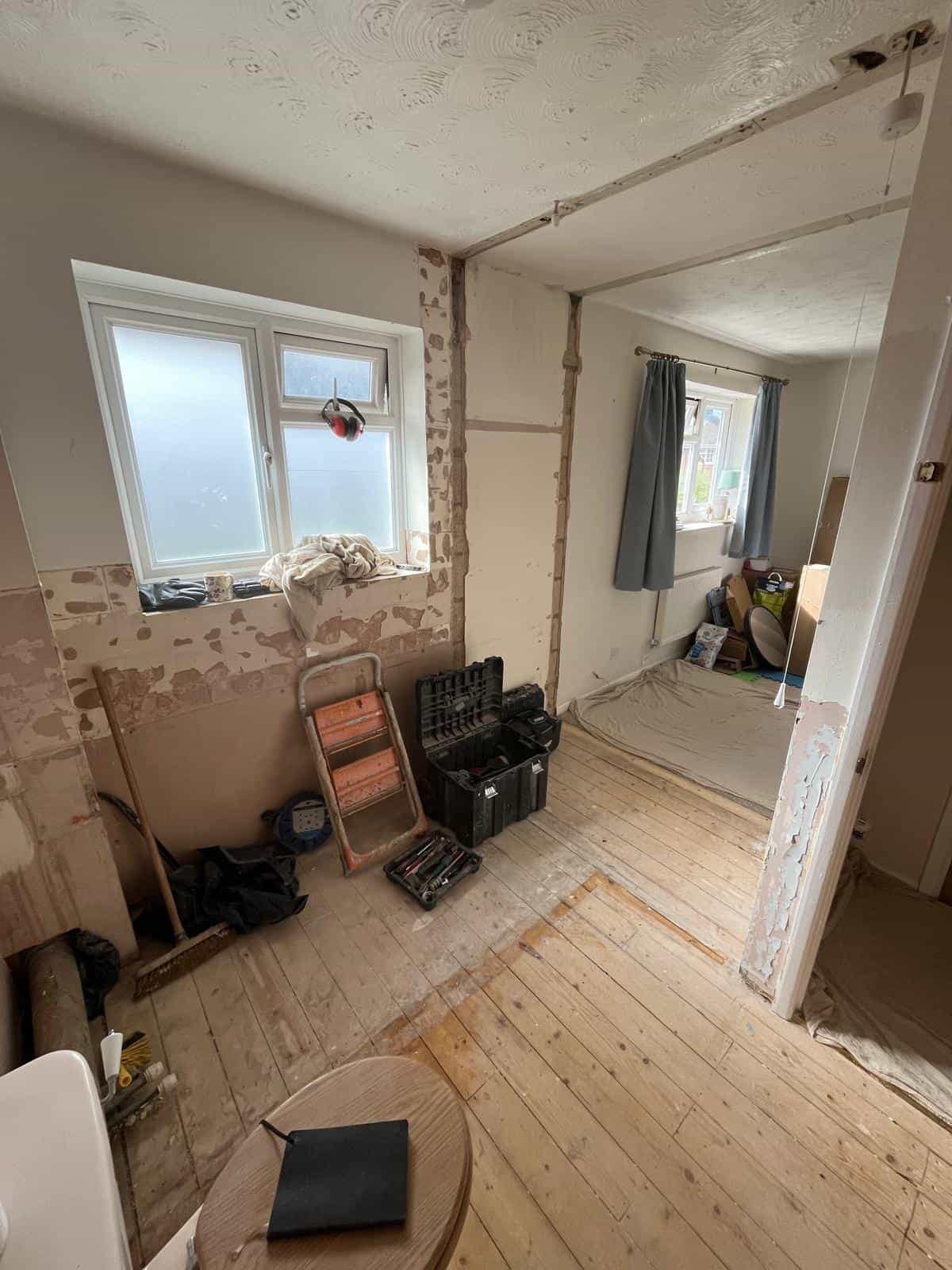 Home Bathroom in Gloucester stripped back for refurbishment, with exposed wooden floorboards, partially removed wall coverings and visible pipework